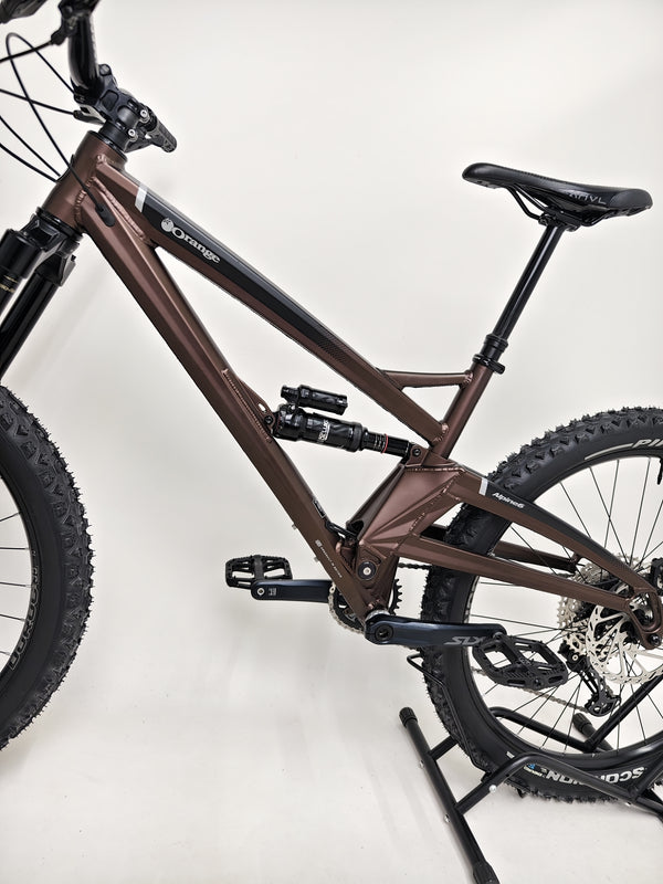 The Orange ALPINE 6 mountain bike parked against a backdrop of rugged cliffs.