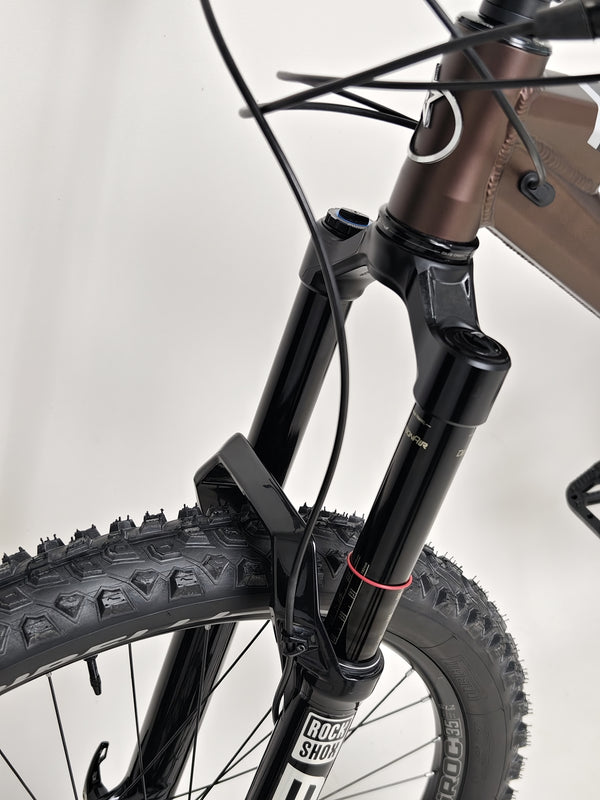 The Orange ALPINE 6 mountain bike balanced on a rock formation, emphasizing its toughness.