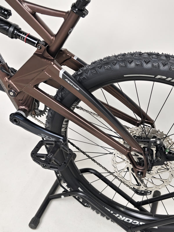 Orange ALPINE 6 mountain bike positioned against a classic stone wall, blending old and new.