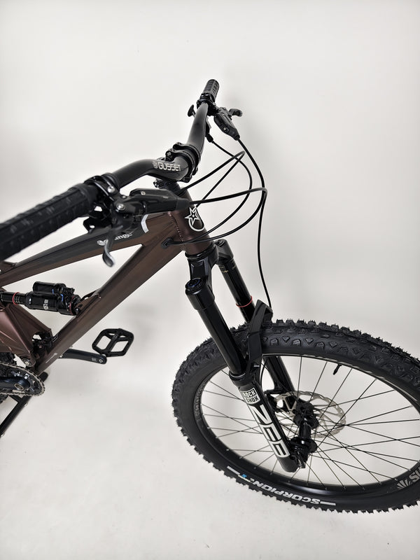 Profile view of the Orange ALPINE 6 mountain bike, reinforced chassis on a biking trail.