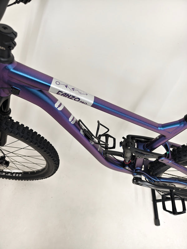 Dynamic action shot of the Voodoo CANZO Pro 2026 LARGE Dropper bike navigating rough terrain, emphasizing its all-mountain capability and Like NEW status.