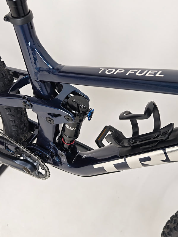 Trek Top Fuel 8 2024 Large Frame Full Suspension Bike at eMado - Detailed image of the bike resting on a scenic background.